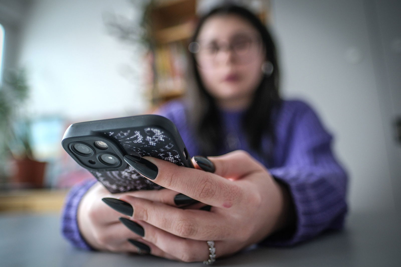 Eine weiblich gelesene, junge Person ist unscharf erkennbar, sie hält ein Handy in Händen.