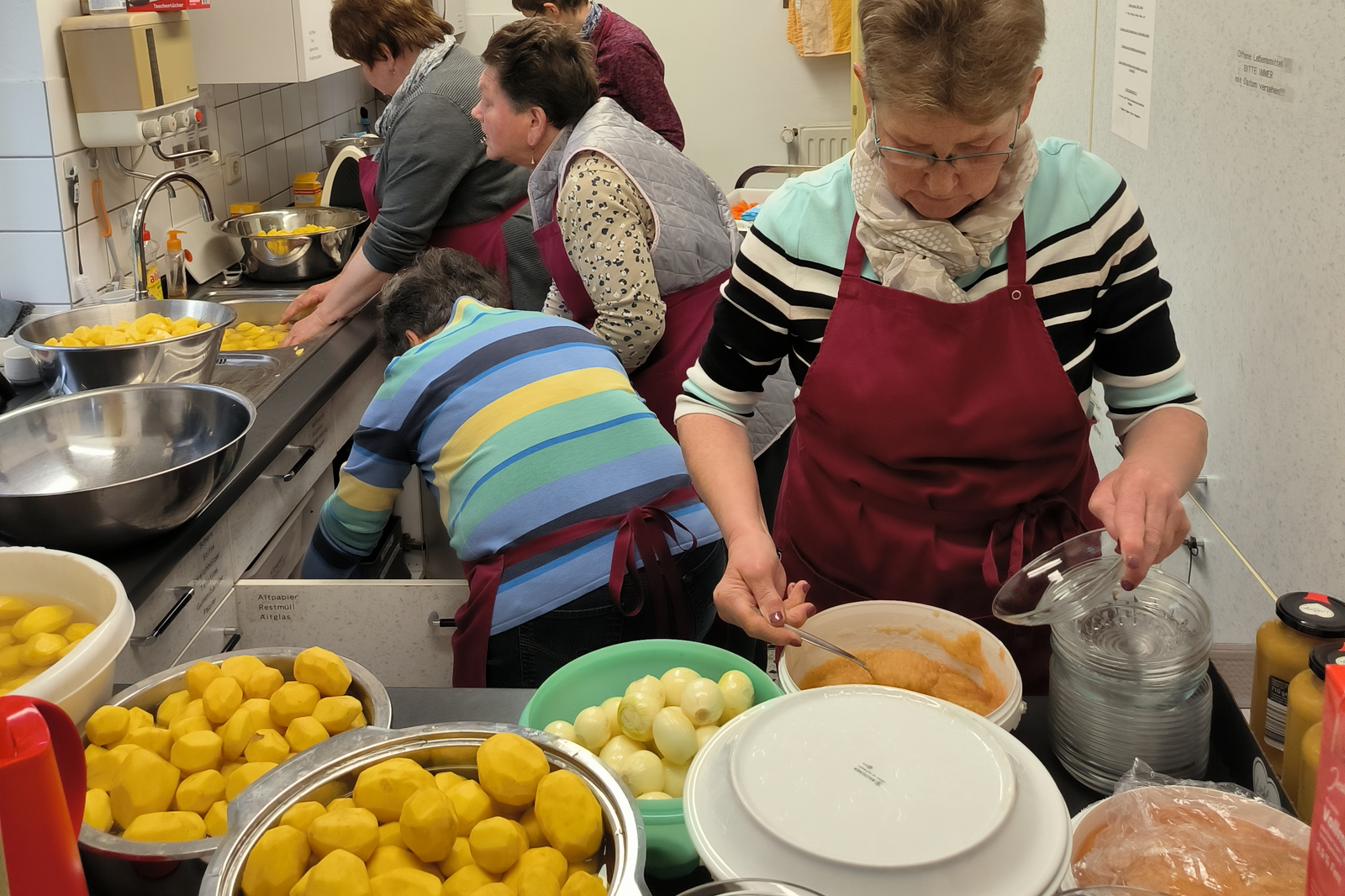 Mehrere Personen in einer kleinen Küche kochen Kartoffeln.