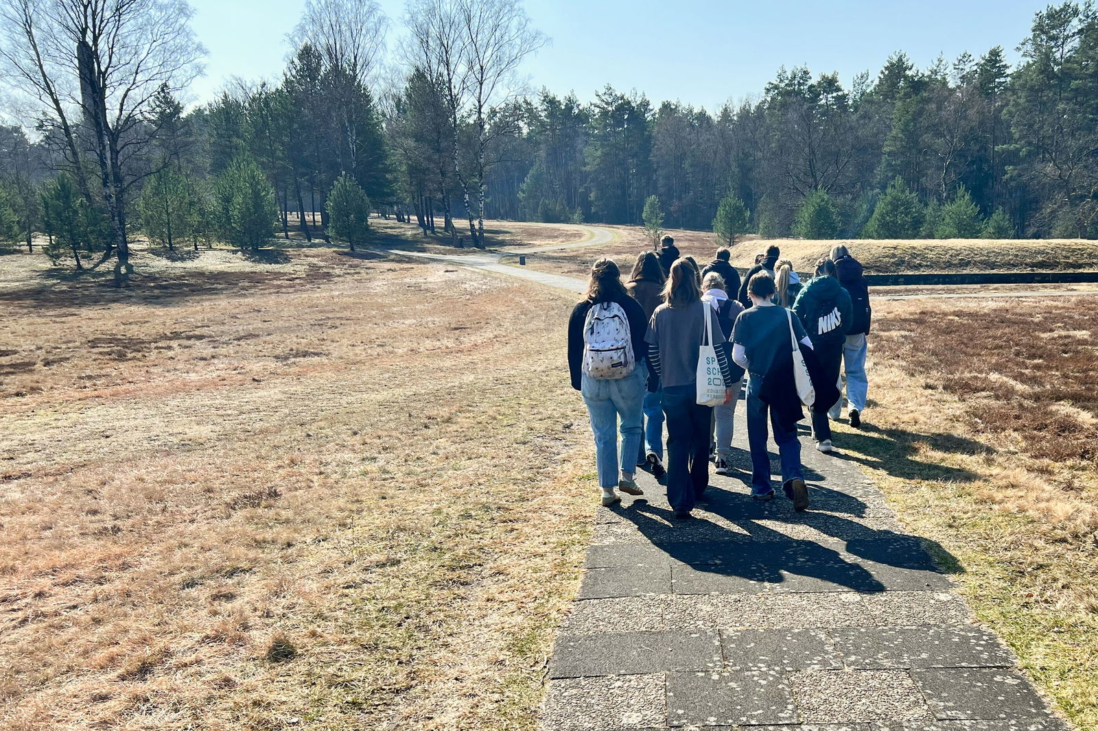 Mehrere junge Menschen gehen auf einem gepflasterten Weg durch eine karge Landschaft.