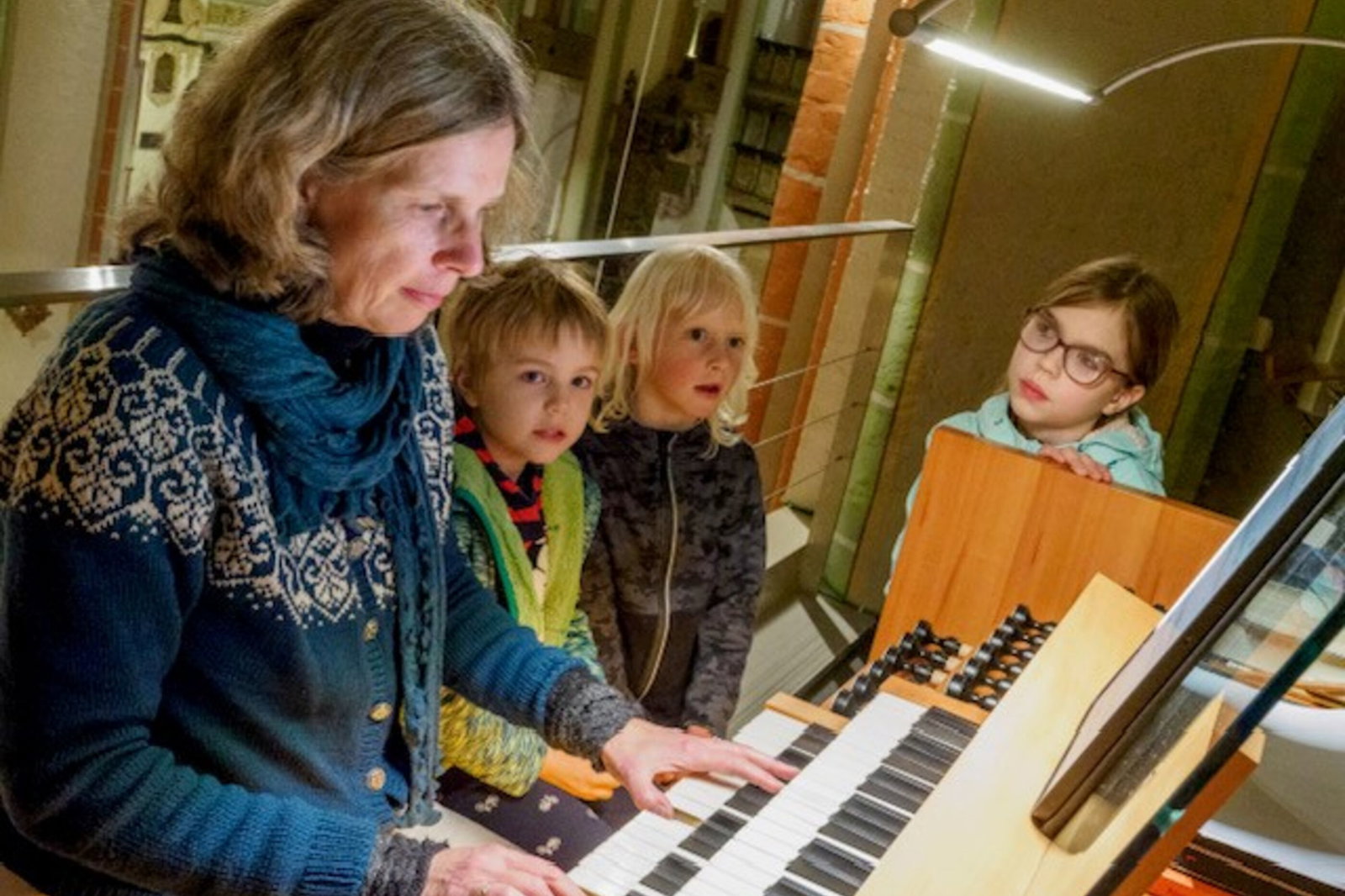 Eine erwachsene Person spielt auf einer Orgeltastatur, drei Kinder schauen zu.