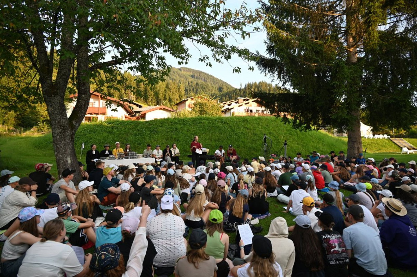 Viele junge Menschen sitzen im Grünen bei einer Andacht zusammen.