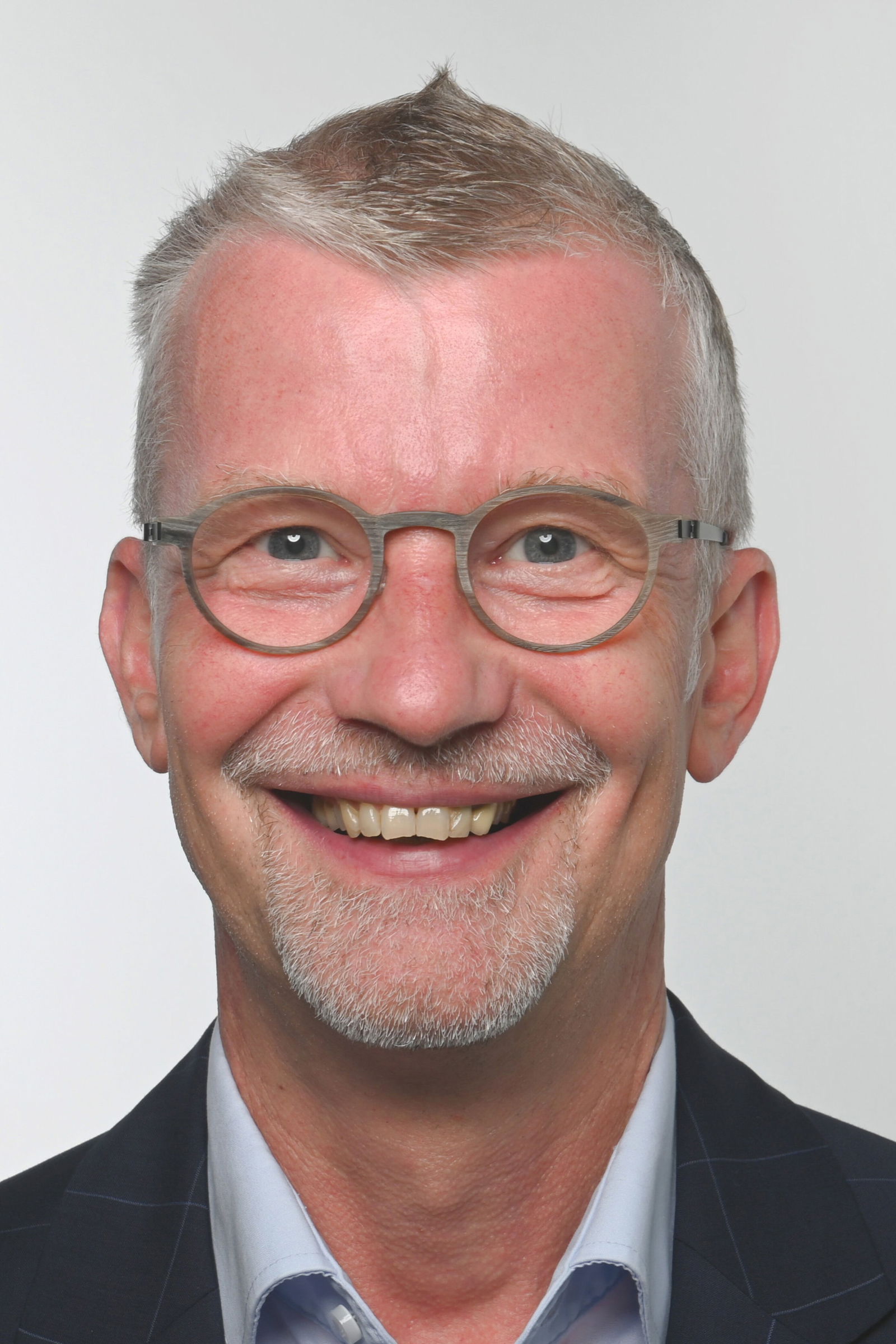 Eine als männlich lesbare Person mit graumelierten Haaren, Dreitagebart und Brille lächelt in die Kamera.