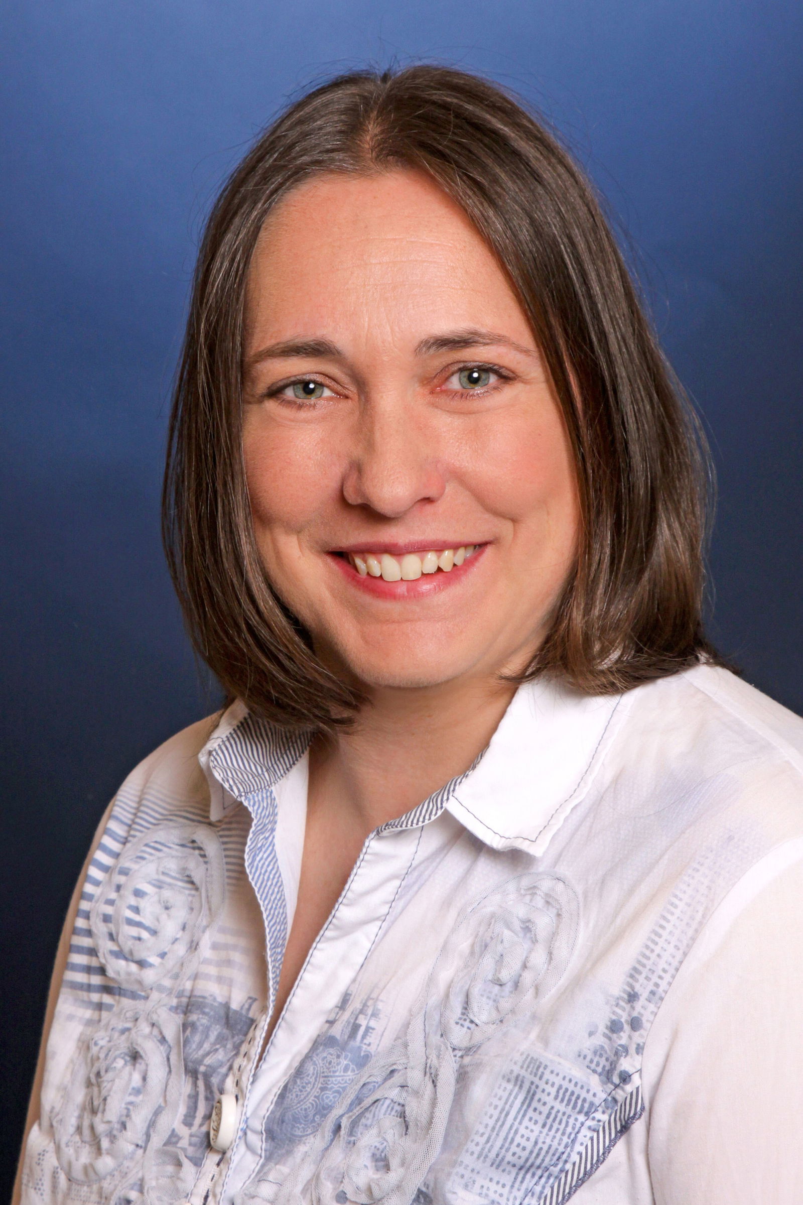 Eine junge Frau mit schulterlangen braunen Haaren und weißem Hemd lächelt in die Kamera.