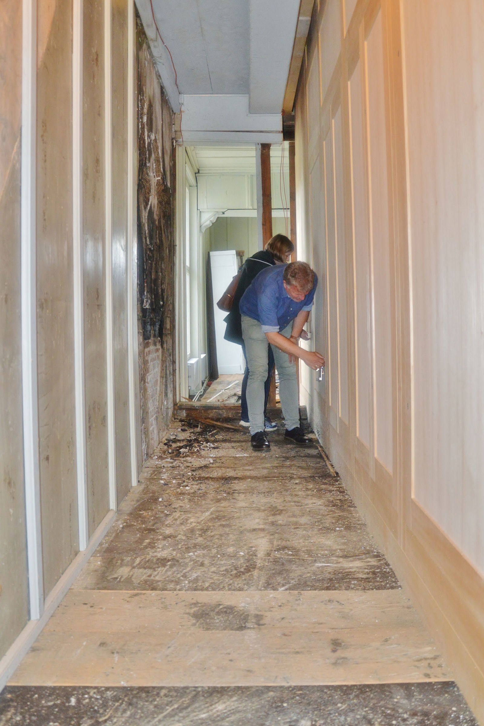 Eine Person steht gebückt zwischen einer Wand, die Brandschäden hat, und einer Holzverkleidung.