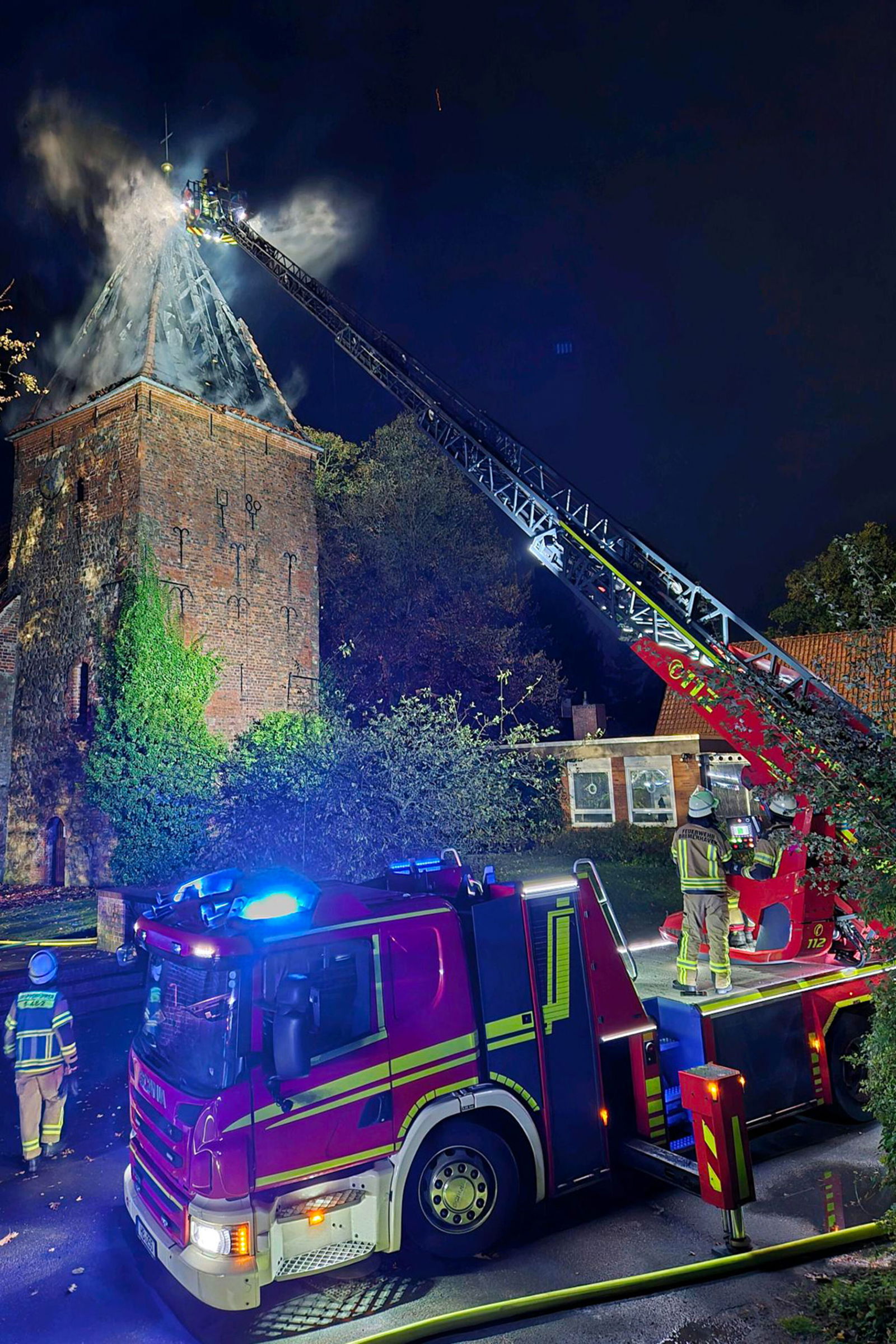 Ein runtergebrannter Kirchturm, davor ein Feuerwehrauto mit ausgefahren Drehleiter