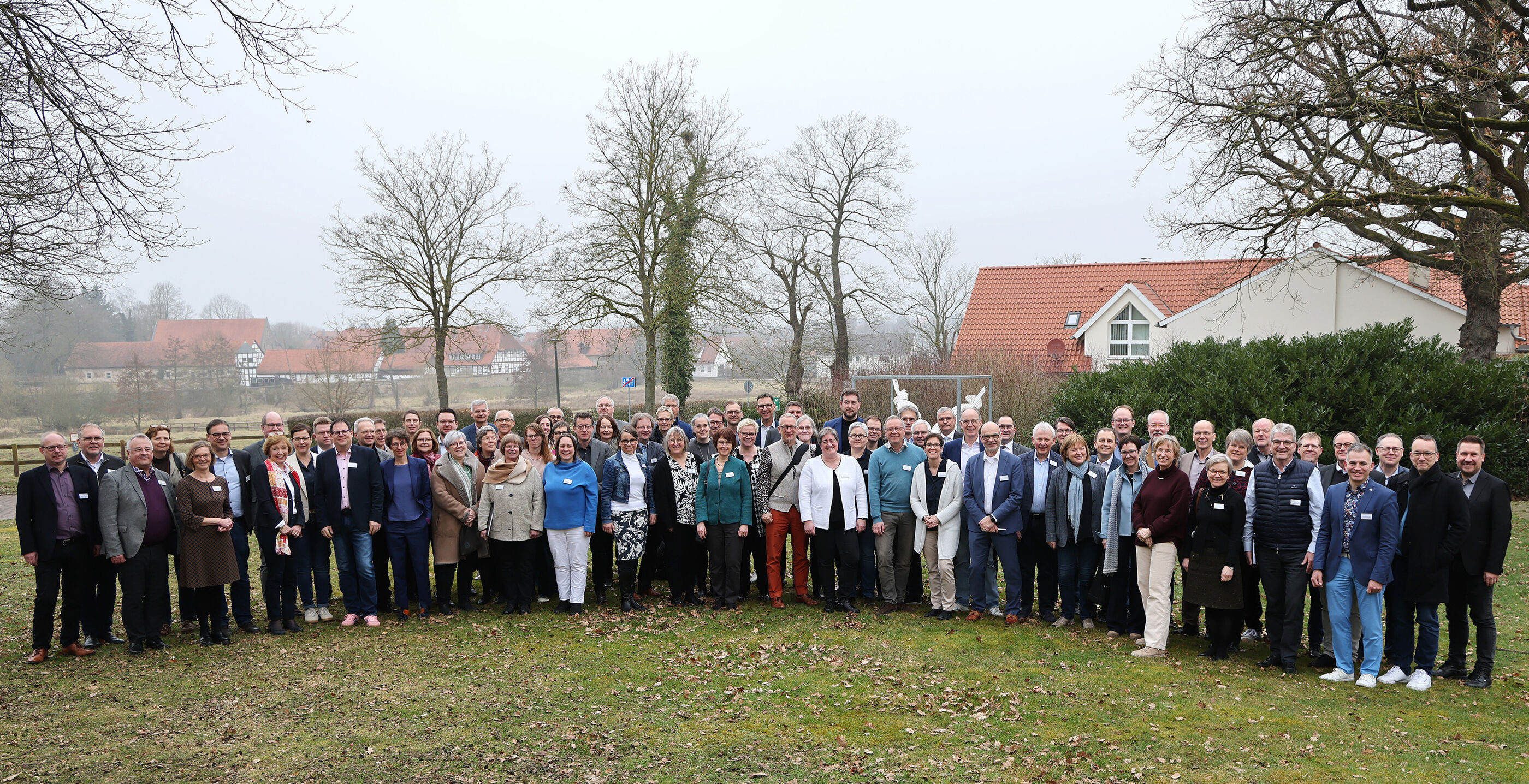 Eine große Gruppe aus als Männer und Frauen lesbare Personen steht auf einer Wiese.