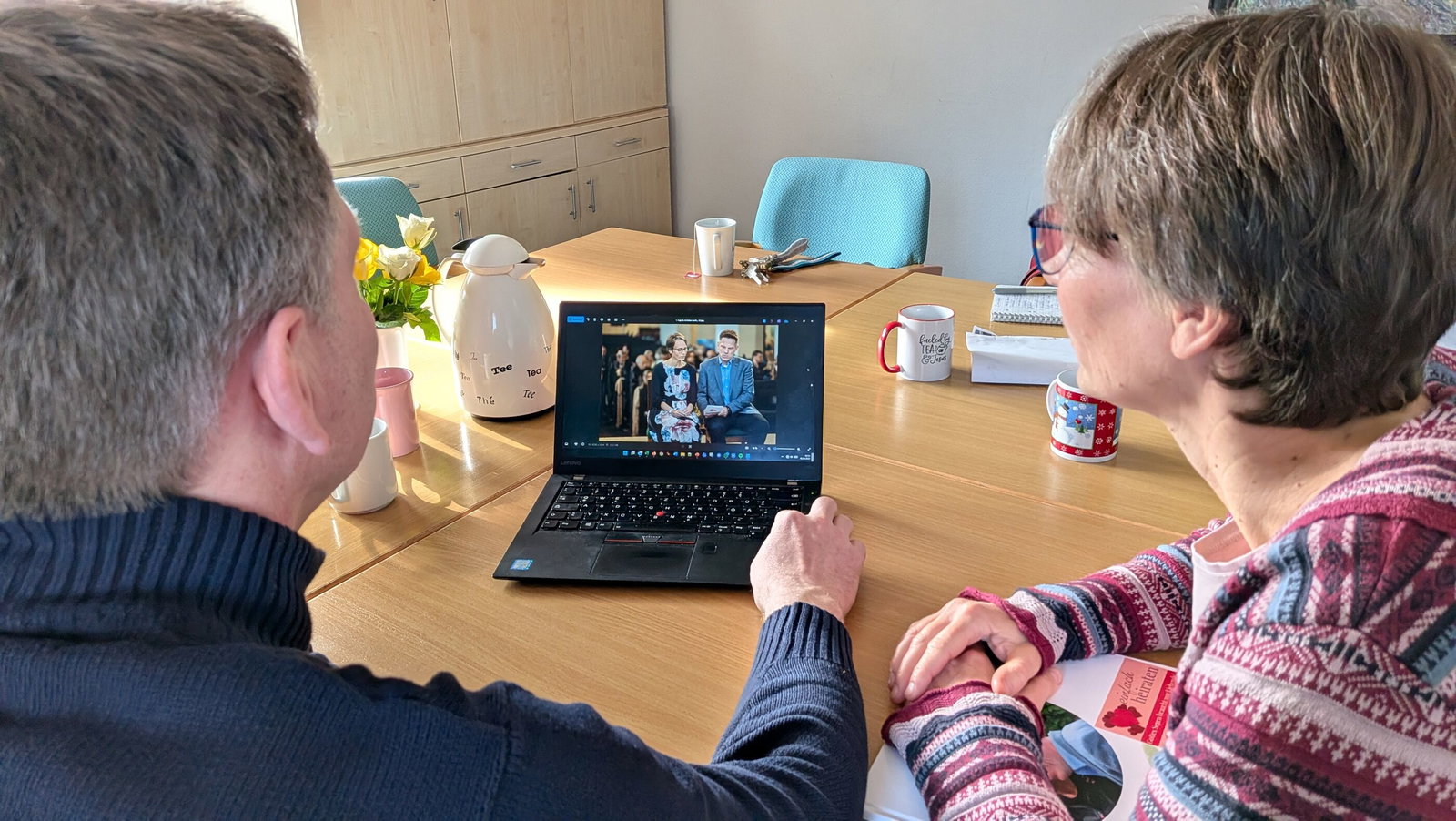 Zwei Personen sitzen an einem Tisch und sehen Hochzeitsbilder an einem Laptop an.