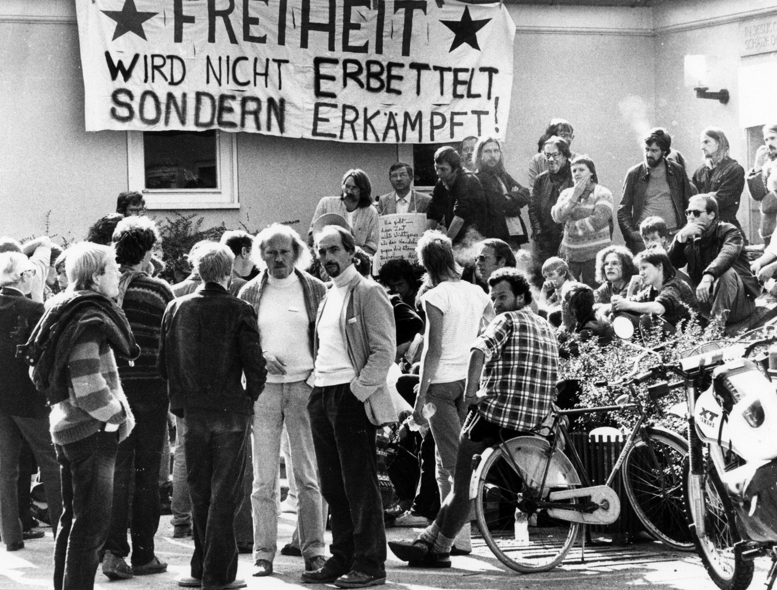 Eine historische Aufnahme mit einer Gruppe, die mit Transparenten vor einem Haus demonstriert.