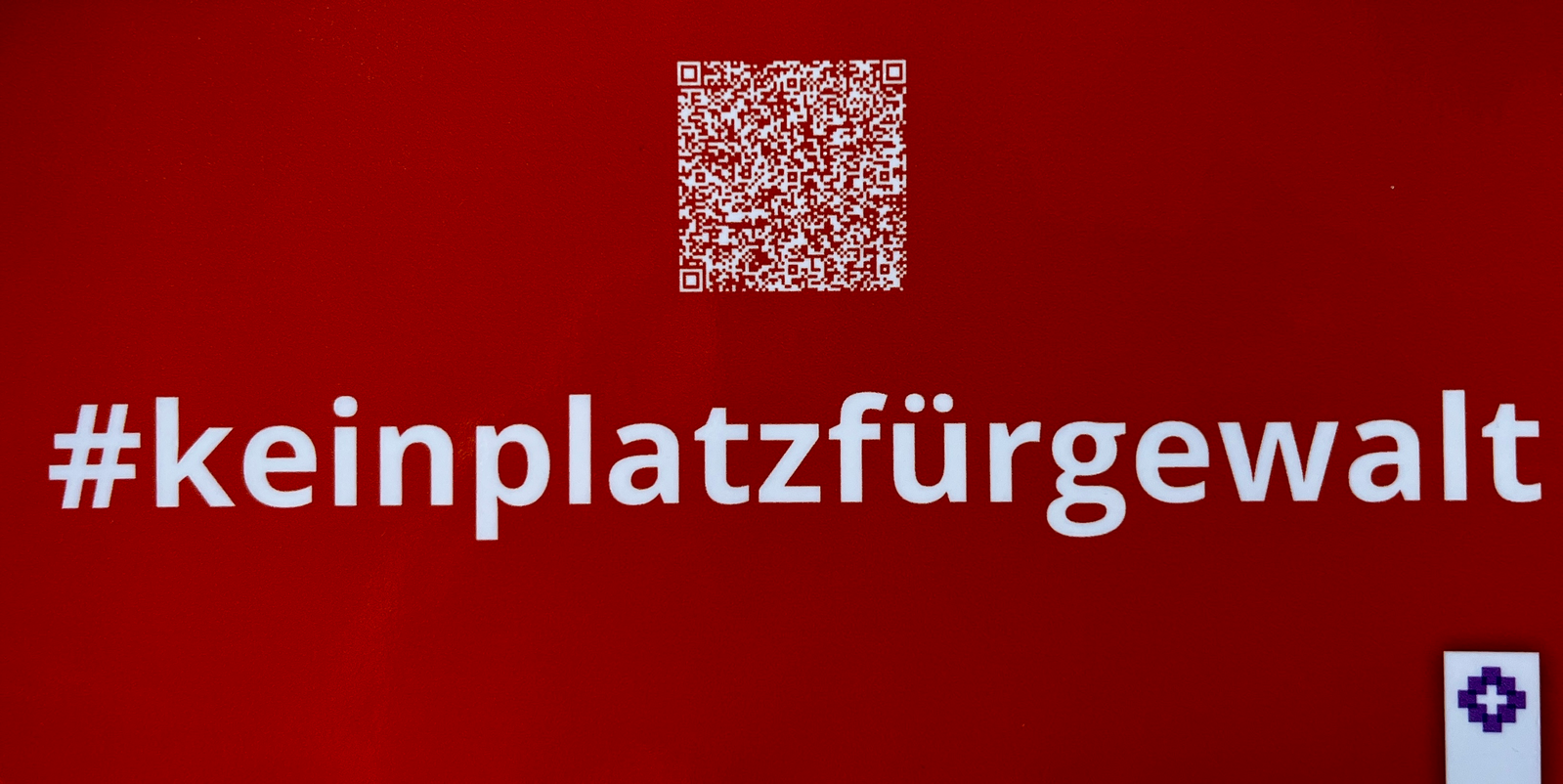 Ein orangefarbener Aufkleber mit weißer Schrift: #keinplatzfürgewalt und darüber ein QR-Code