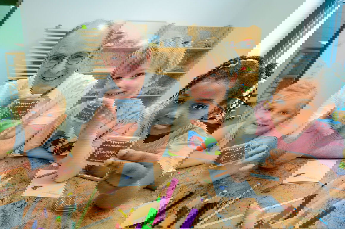 Eine als Mann lesbare mittelalte Person und drei Kinder halten einen kleinen Radierer in die Kamera.