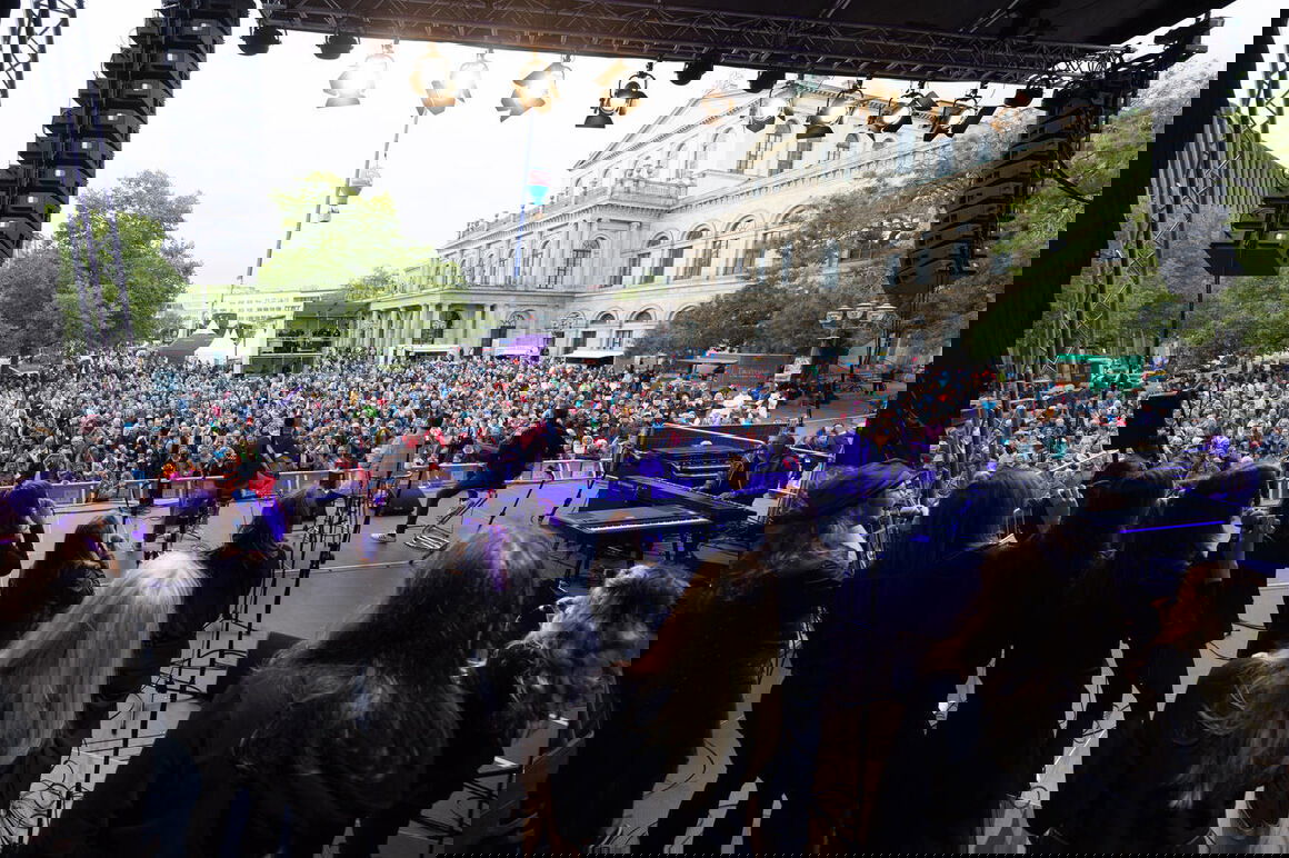 Blick vom hinteren Ende einer Bühne über Personen auf der Bühne hinweg auf ein großes Publikum.