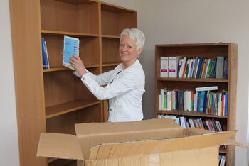 Landespastorin Susanne Briese räumt die Regale in ihrem neuen Büro im HkD ein. Bild: Gunnar Schulz-Achelis / HkD