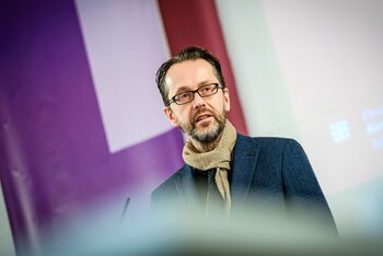 Eine männlich lesbare Person an einem Rednerpult