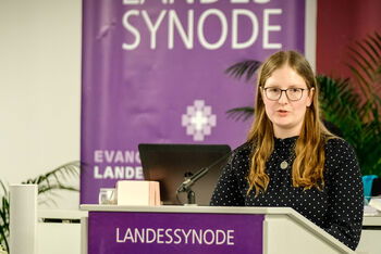 Eine weiblich lesbare Person steht am Podium und spricht.