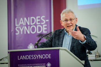 Eine männlich lesbare Person steht am Rednerpult und spricht.