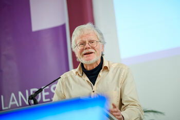 Eine männlich lesbare Person steht am Rednerpult und spricht