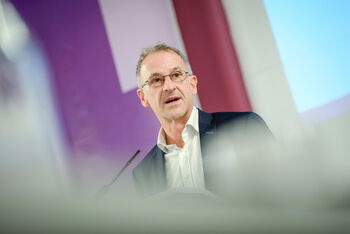 Eine männlich gelesene Person mit Brille und kurzen Haaren am Podium.