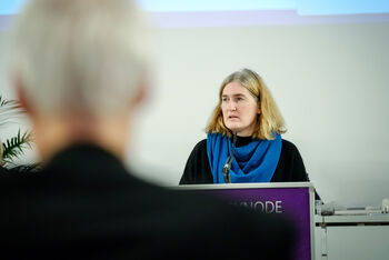 Eine weiblich lesbare Person steht am Podium und spricht.