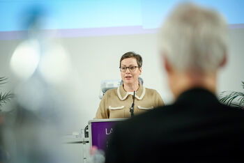 Eine weiblich lesbare Person steht am Podium und spricht.