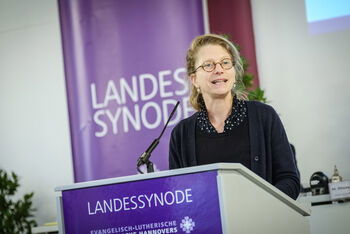 Eine weiblich lesbare Person steht an einem Rednerpult und spricht