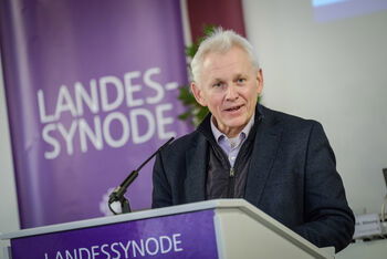 Eine männlich lesbare Person steht an einem Rednerpult und spricht