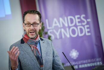 Eine männlich lesbare Person steht an einem Rednerpult