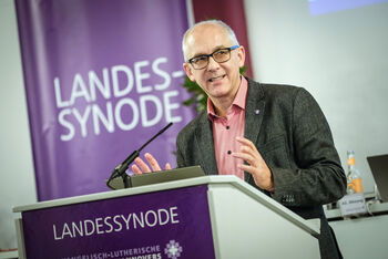 Eine männlich lesbare Person steht an einem Rednerpult und spricht.