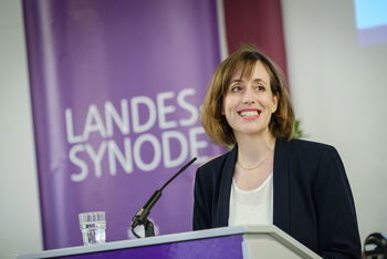 Eine weblich lesbare Person steht an einem Rednerpult und spricht