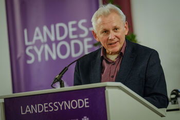 Eine männlich lesbare Person steht an einem Pult und hält eine Rede.