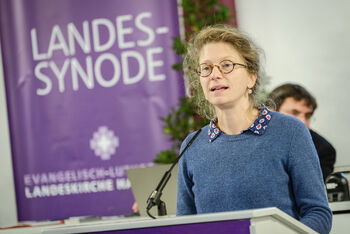 Eine weiblich lesbare Person steht an einem Rednerpult