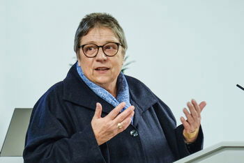 Eine weiblich lesbare Person steht an einem Pult und redet.