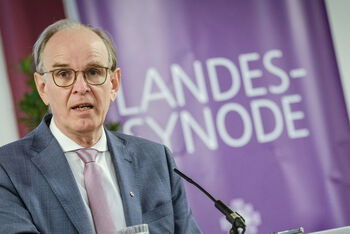 Eine männlich lesbare Person im grauen Anzug am Rednerpult.