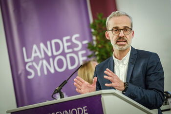 Eine männlich lesbare Person steht an einem Rednerpult und spricht.