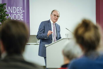 Eine männlich zu lesende Person an einem Redepult.