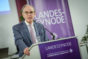 Eine männlich zu lesende Person steht an einem Redepult.