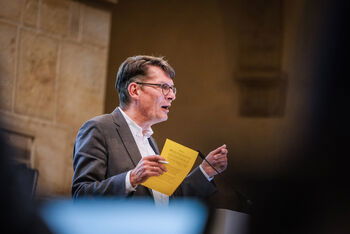 Eine männlich lesbare Person steht an einem Podium und spricht.