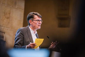 Eine männlich lesbare Person steht an einem Podium und spricht.