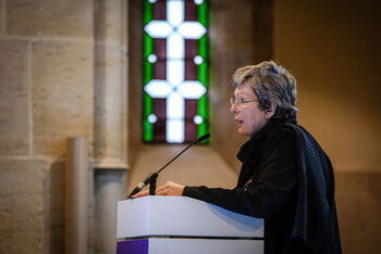 Eine weiblich lesbare Person steht an einem Podium und spricht.