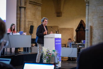 Eine weiblich gelesene Person steht vor einem Redepult.