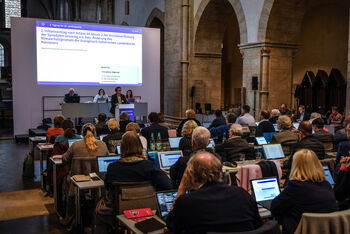 Mehrere Personen sitzen in einer zum Sitzungssaal umfunktionierten Kirche