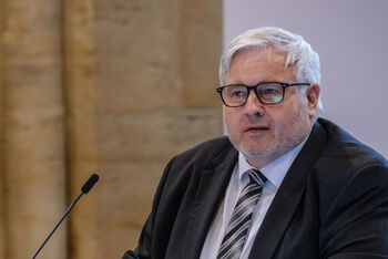 Eine männlich gelesene Person steht vor einem Redepult.