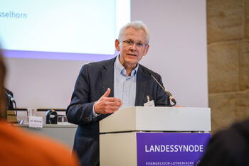 Eine männlich gelesene Person steht vor einem Redepult.