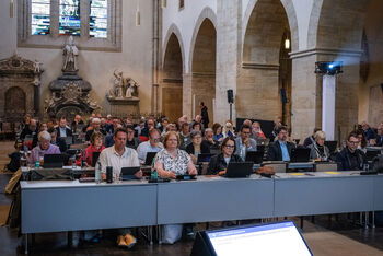 Mehrere Menschen sitzen in einer Kirche und hören der vortragenden Person zu.