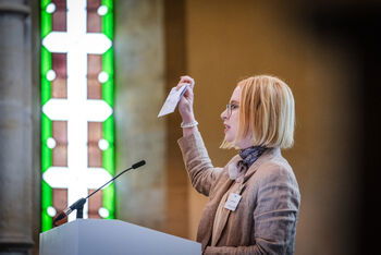 Eine weiblich lesbare Person steht an einem Podium und spricht.