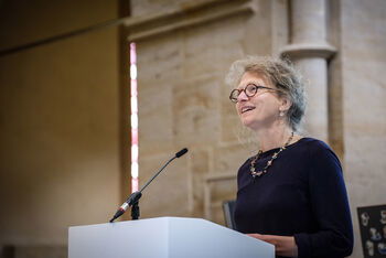 Eine weiblich lesbare Person steht an einem Podium und spricht.