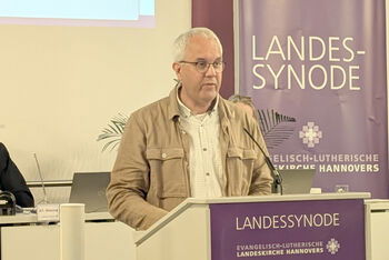 Eine männlich zu lesende Person spricht am Redepult in ein Mikrofon.