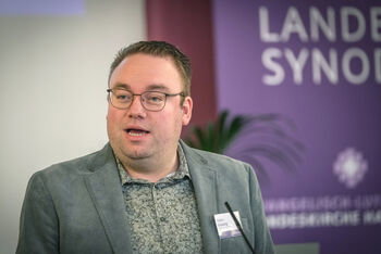 Eine männlich lesbare Person an einem Rednerpult