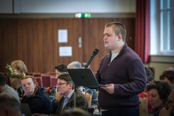 Eine männlich lesbare Person an einem Mikrofon