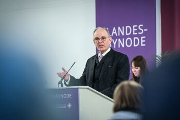 Eine als Mann lesbare Person hält an einem Pult eine Rede.