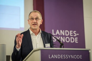 Eine als Mann lesbare Person mittleren Alters spricht an einem Redepult.